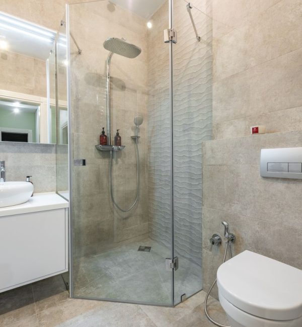 Contemporary shower room between cabinet with washstand and toilet bowl on tiled floor at home